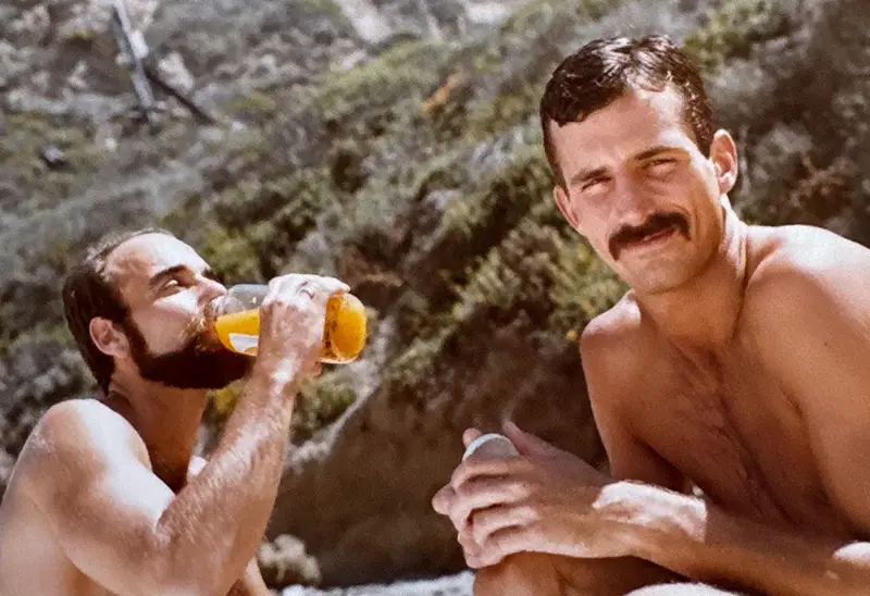 Tommy and Roger lounging on beach with jug of orange juice